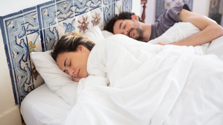 Couple asleep side by side in a bedroom with a decorative tile headboard