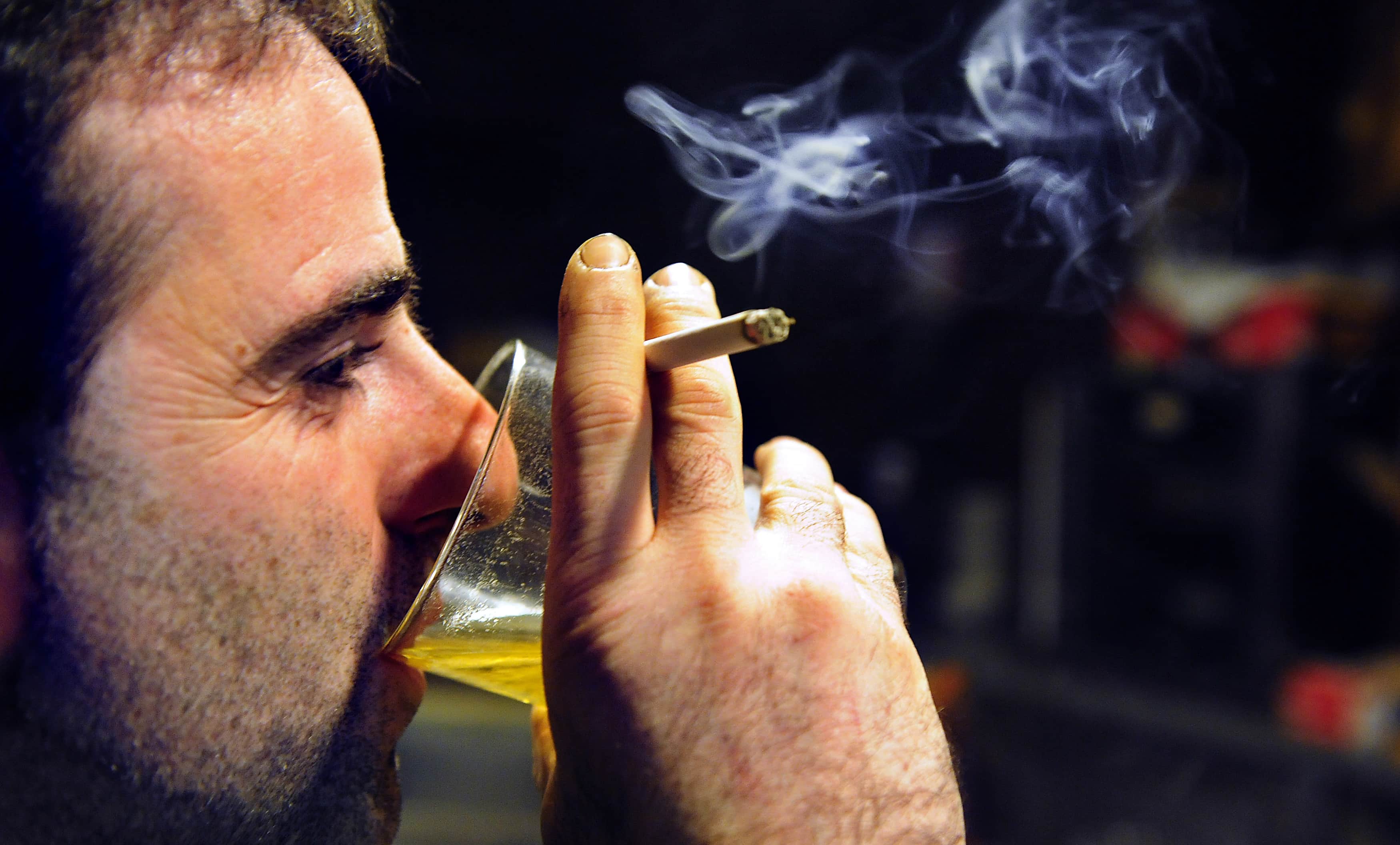 A man drinks beer while smoking a cigarette