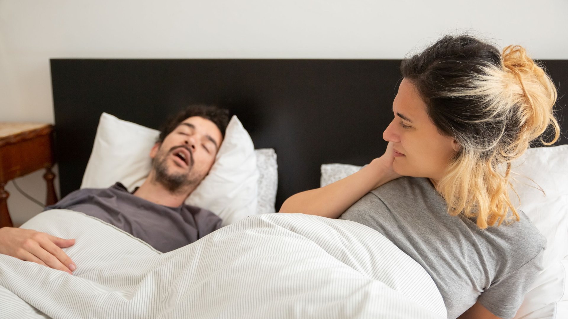 Man sleeping with his mouth open next to a woman lying awake in bed