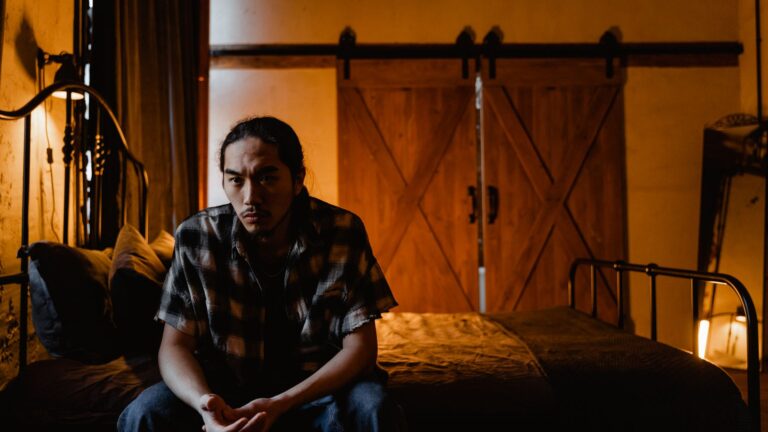 Pensive man sitting on the edge of his bed in a dim room