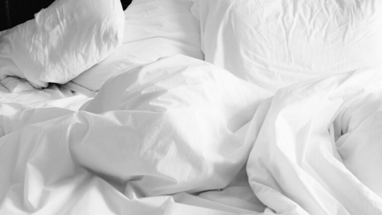 Rumpled white bedding and pillow on an unmade bed