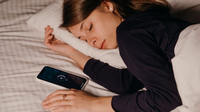 Woman asleep on her side with a smartphone on the sheet beside her
