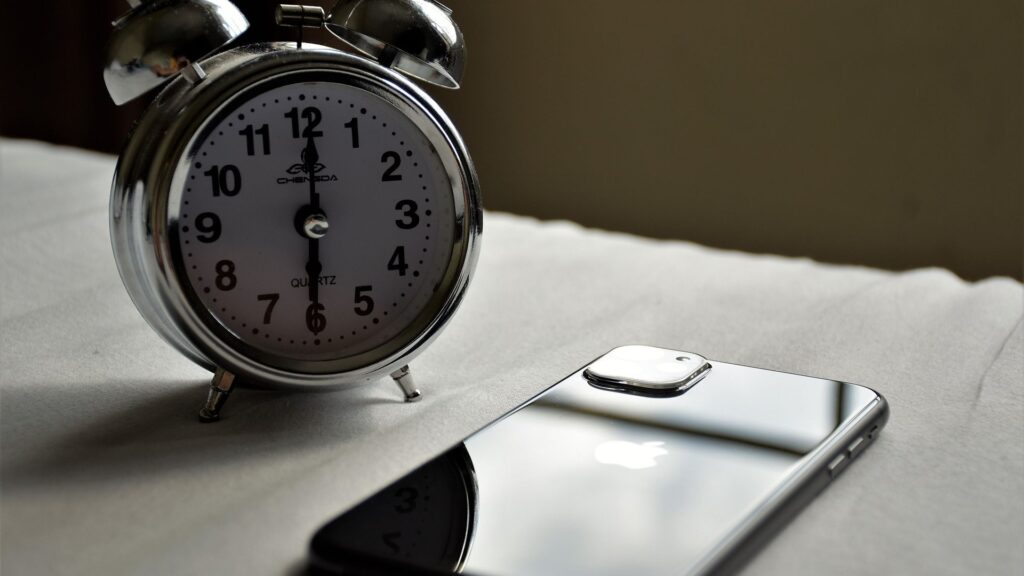 Vintage alarm clock beside a black smartphone on a bedside table