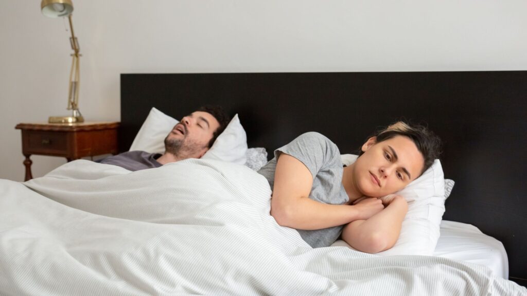 Woman lying awake in bed next to her snoring partner