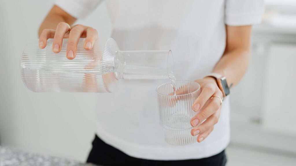 Person pouring water from a glass carafe into a drinking glass