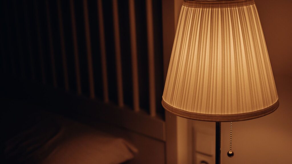 Pleated bedside lamp glowing warmly in a dark bedroom