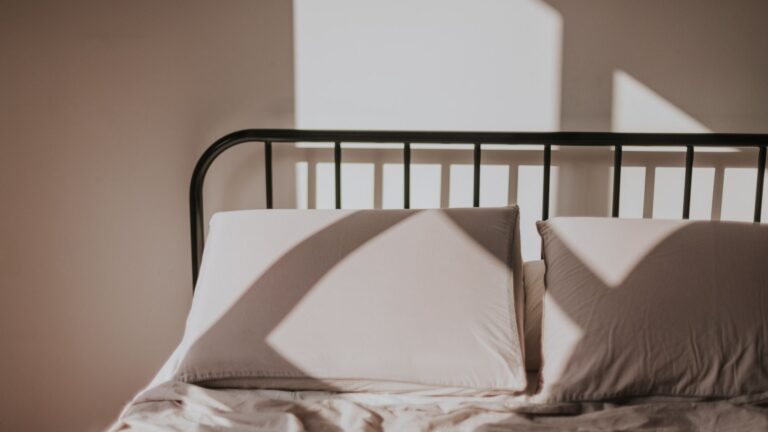 Two pillows on a bed with a black metal frame in morning light