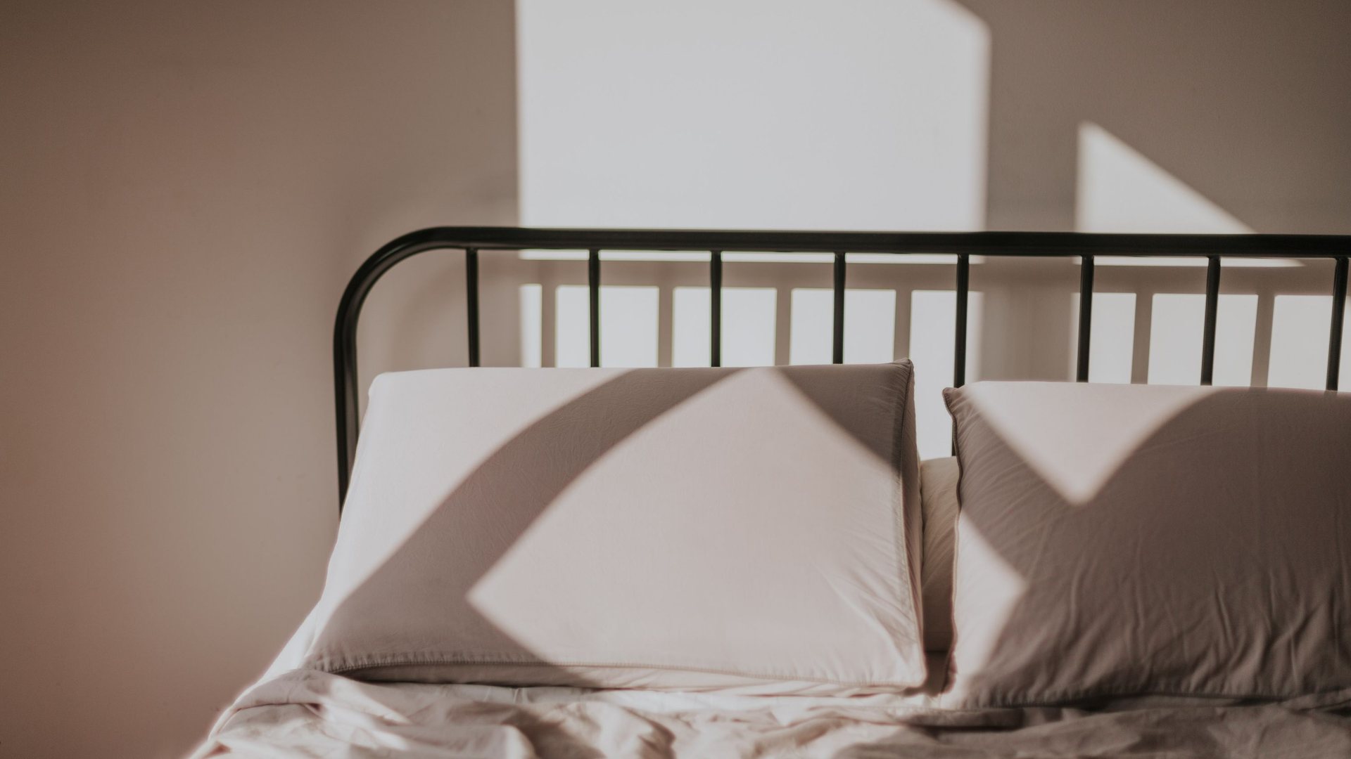 Two pillows on a bed with a black metal frame in morning light